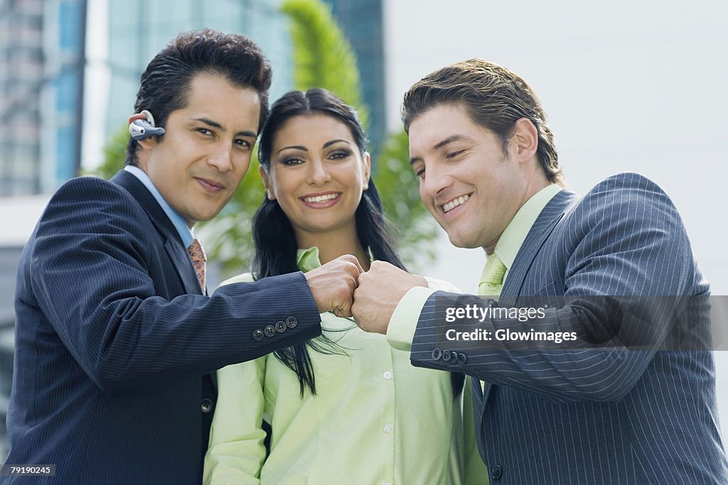 Two businessmen touching knuckles and a businesswoman smiling