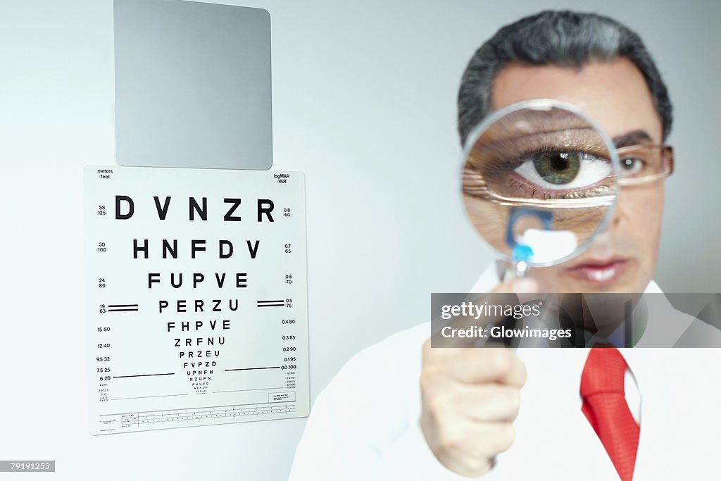 Portrait of a male doctor holding a magnifying glass in front of his eye