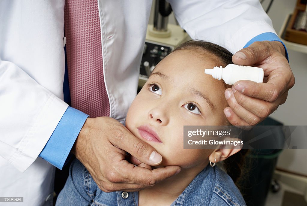 Mid section view of a doctor putting eye drops in a girl's eye
