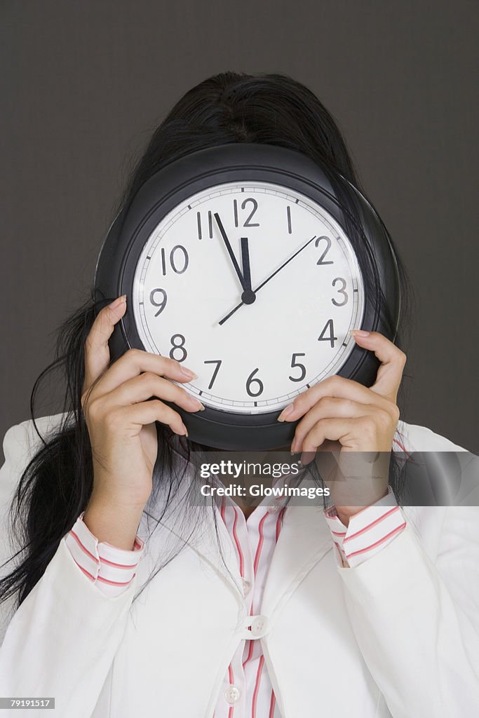 Close-up of a businesswoman holding a clock in front of her face