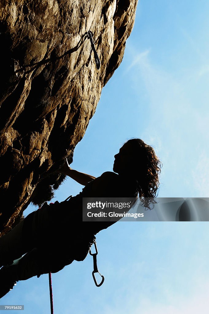 Silhouette of a female rock climber holding onto a rock with the help of a rope