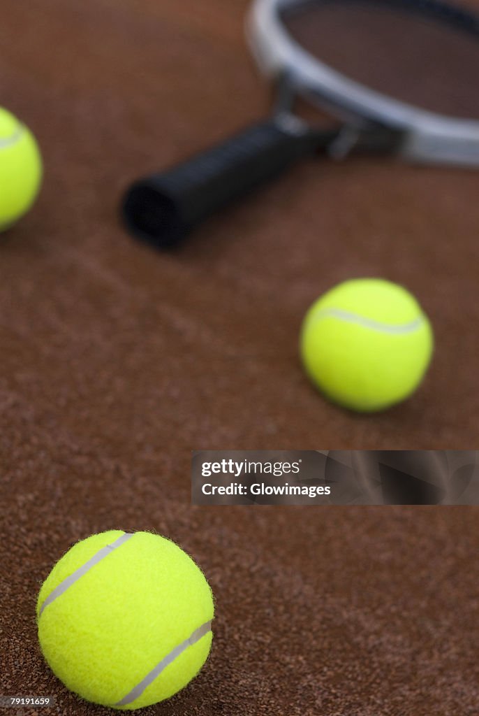 Close-up of three tennis balls and a racket in a court