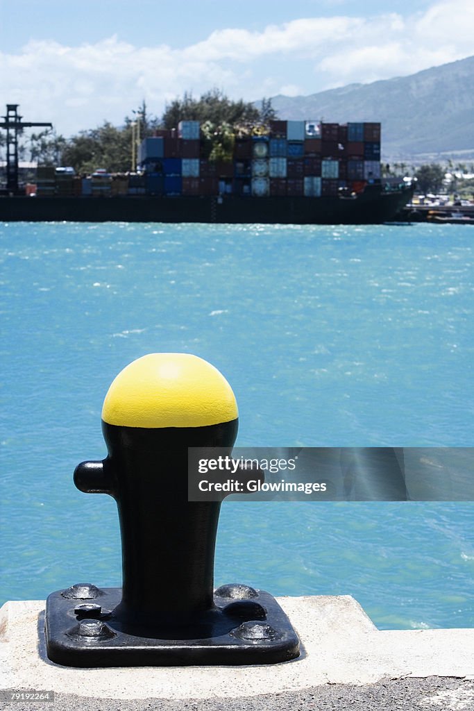 Close-up of a bollard with cargo containers in the background at a commercial dock