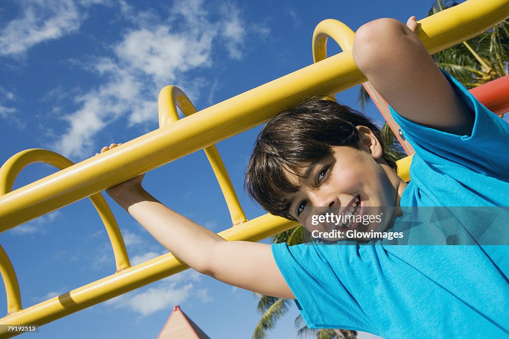 Portrait of a boy hanging on monkey bars and smiling