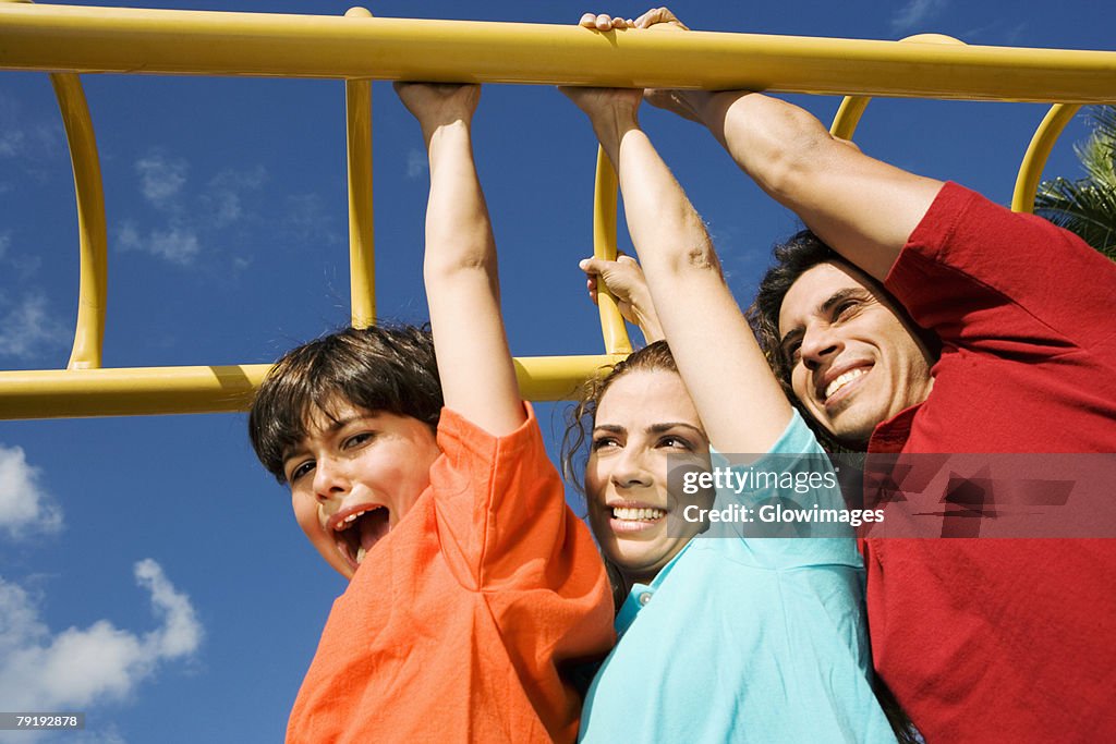 Mid adult couple hanging on monkey bars with their son and smiling