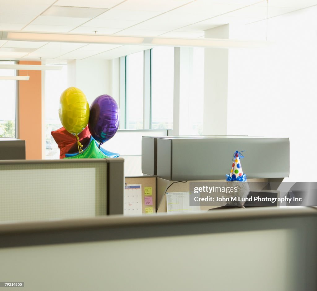 Businessman in a cubicle with a party hat on and a bunch of balloons, Redwood City, California, United States