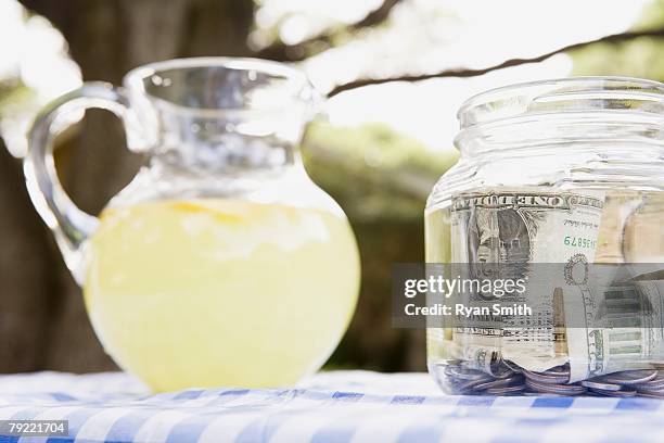 pitcher of lemonade and a money jar - earnings season stock pictures, royalty-free photos & images