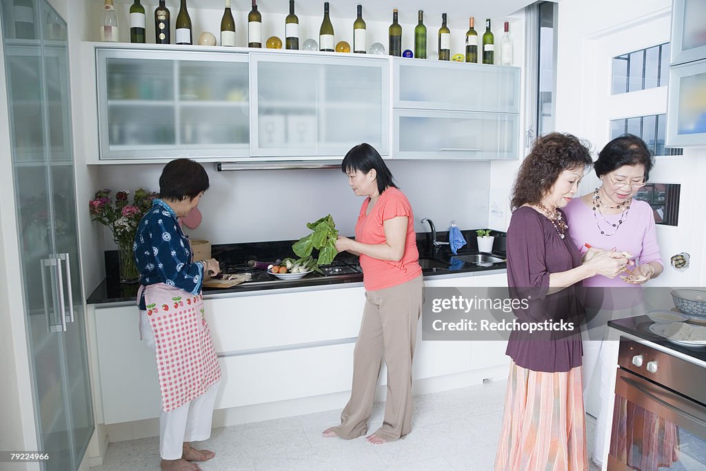 Three senior women and a mature woman preparing food in a domestic kitchen