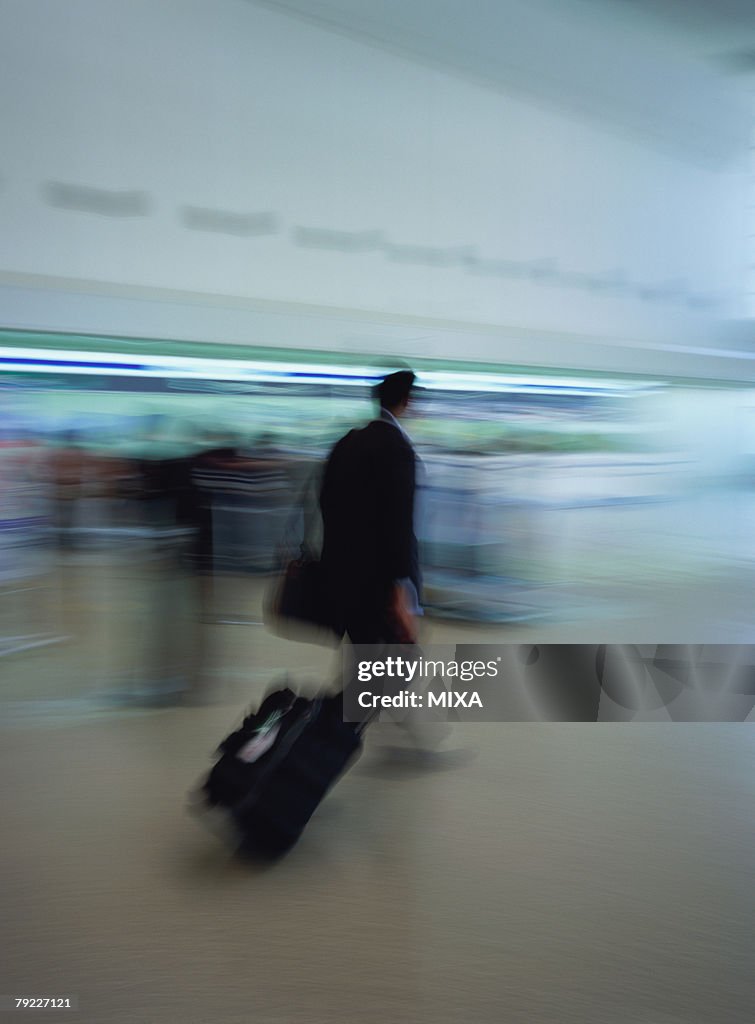 Man walking with luggage at airport, blurred motion