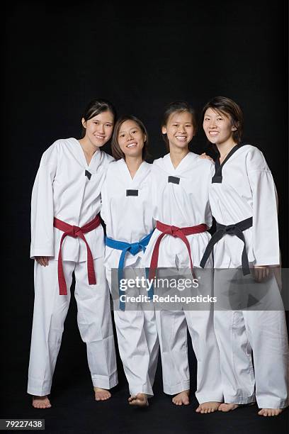 four young women smiling and standing in gi - gi abbigliamento per arti marziali foto e immagini stock