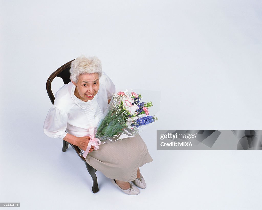 A senior woman sitting in a chair with flower bouquet