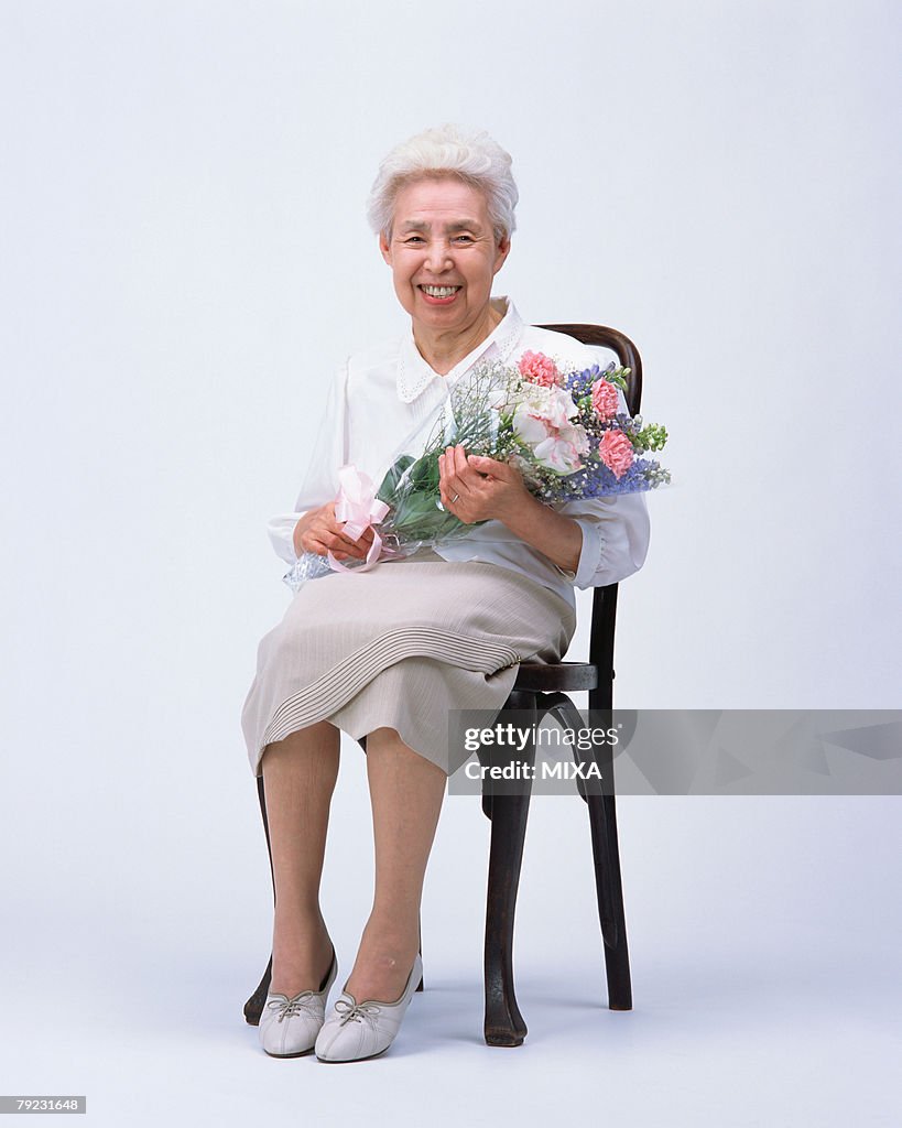 A senior woman sitting in a chair with flower bouquet