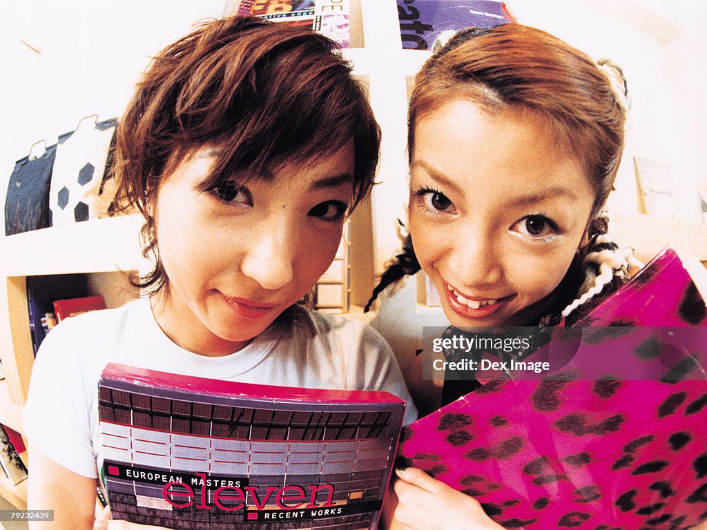 Two young woman smiling, carrying books, close up