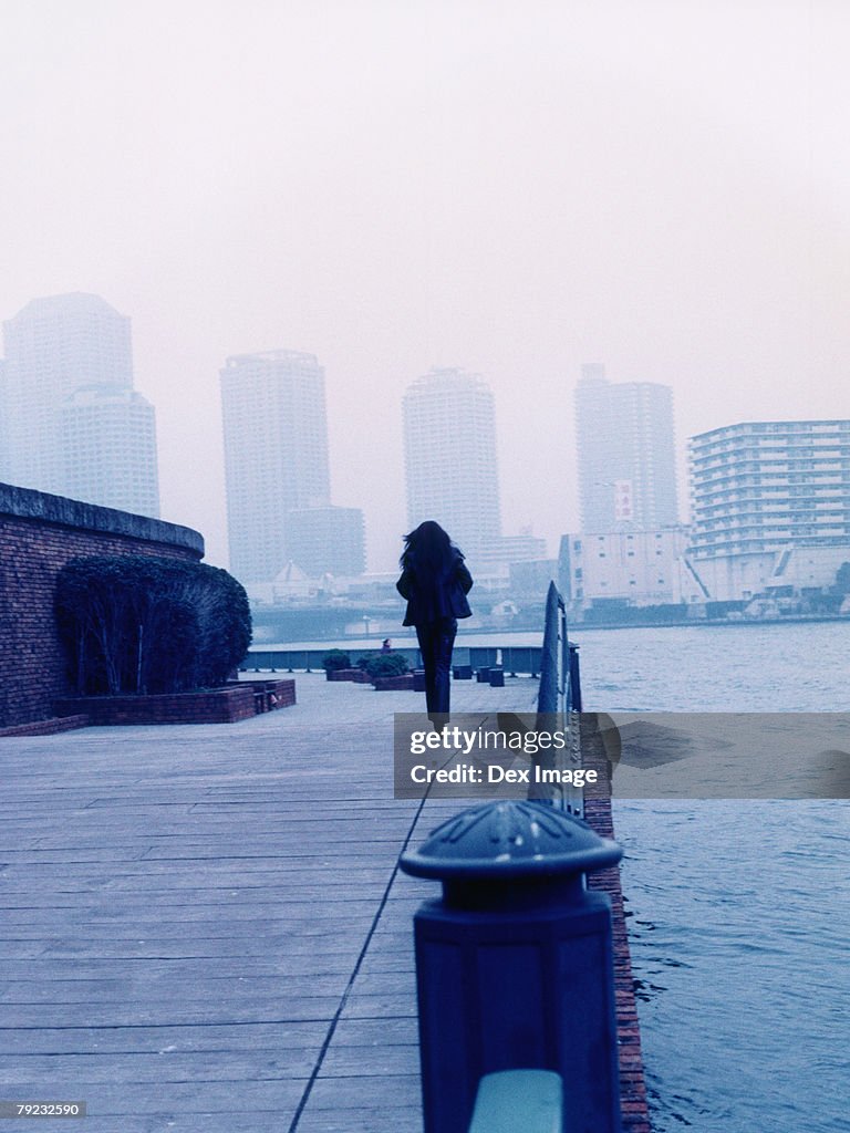 Woman walking along jetty, Tokyo city in background