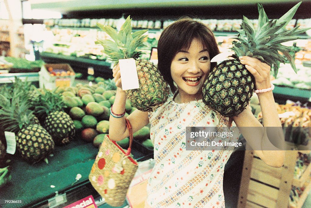 Young woman holding pineapples in fruit store
