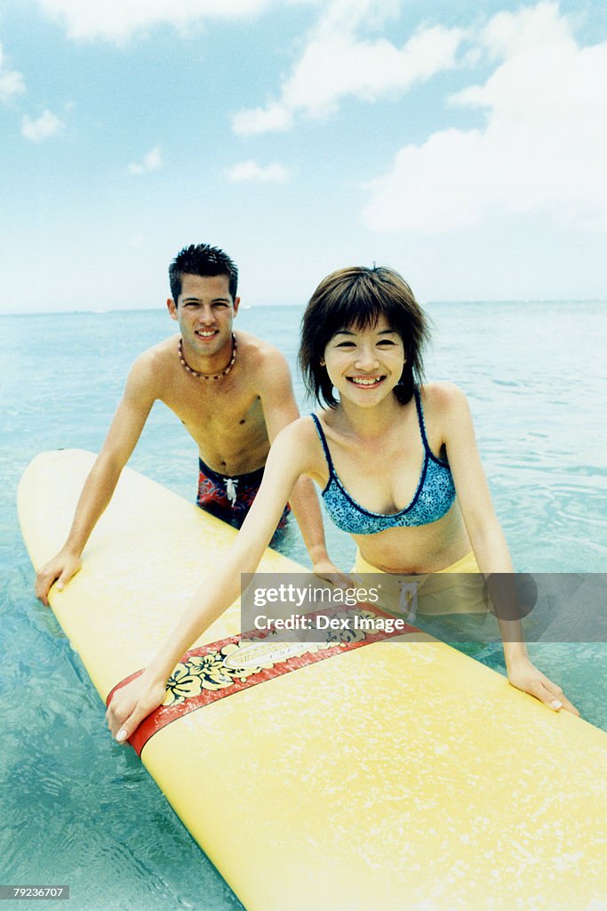 Young man and woman holding surfboard in water