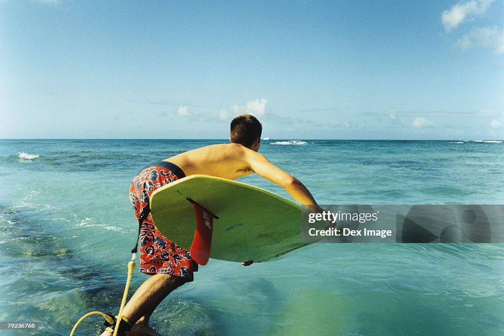 Young man jumping off with surfboard, rear view