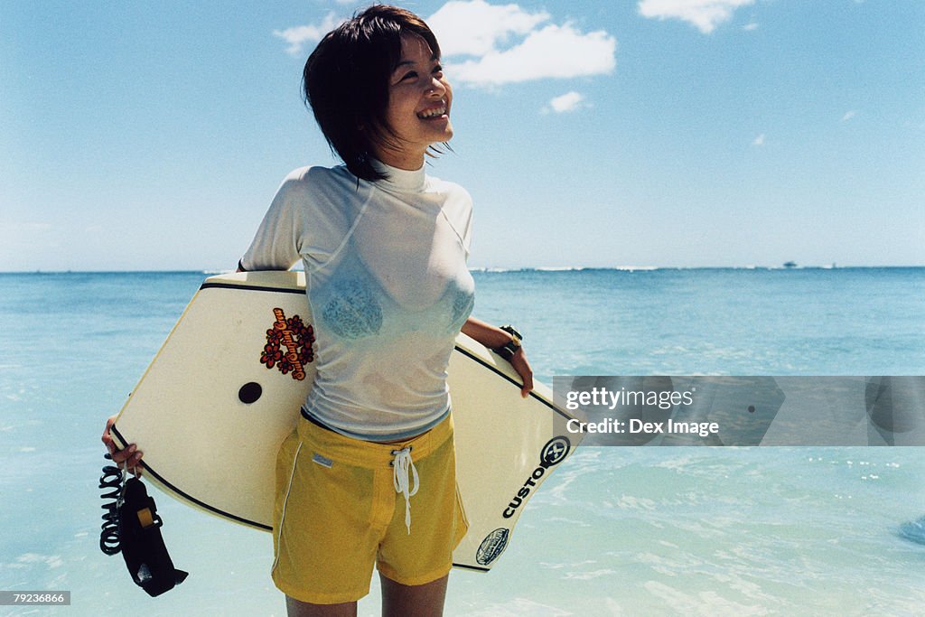 Young woman at a beach, holding paddleboard