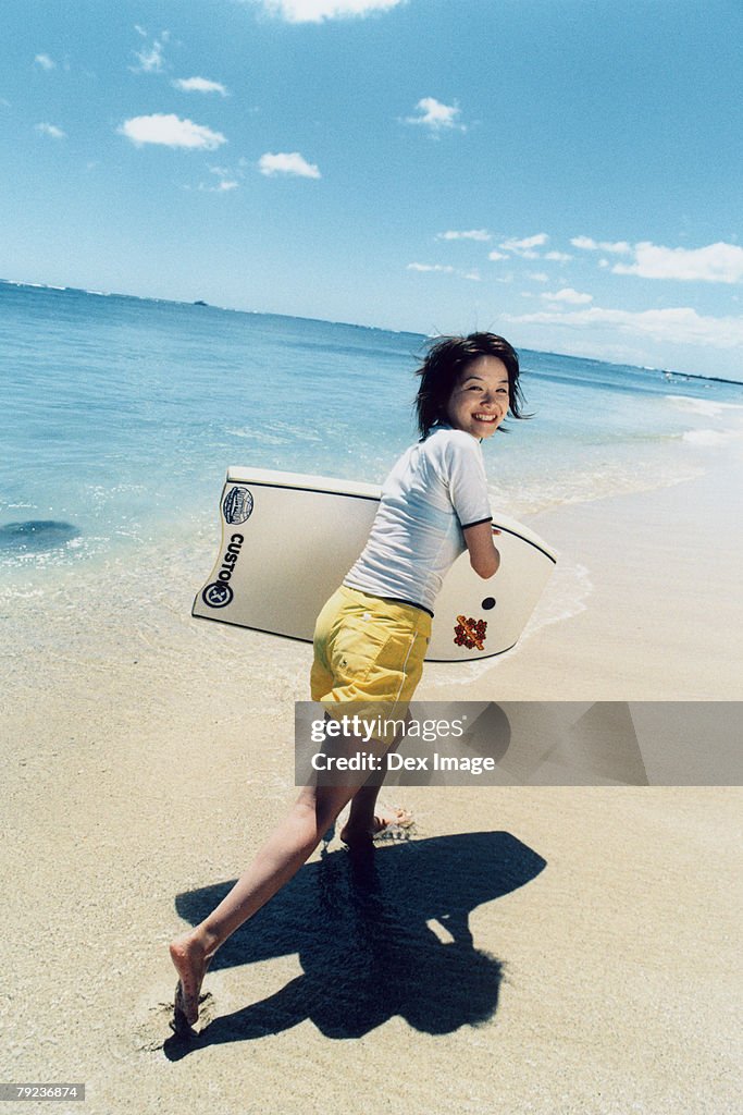 Young woman running at a beach with surfboard