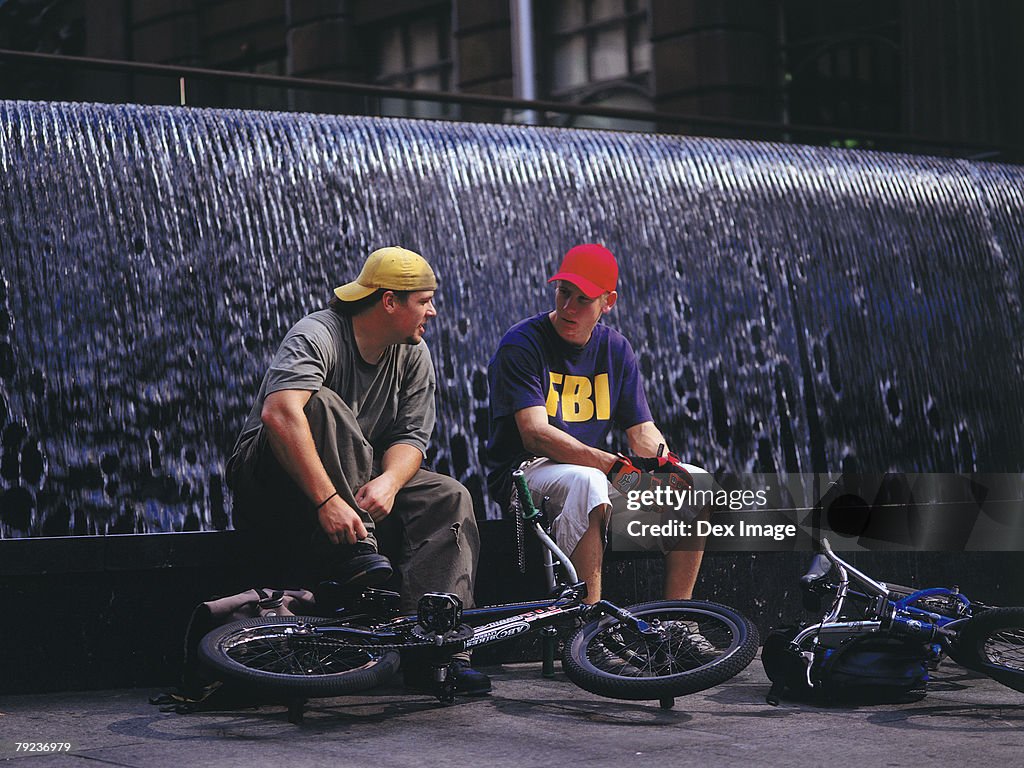 Young men resting on BMX on water fountain