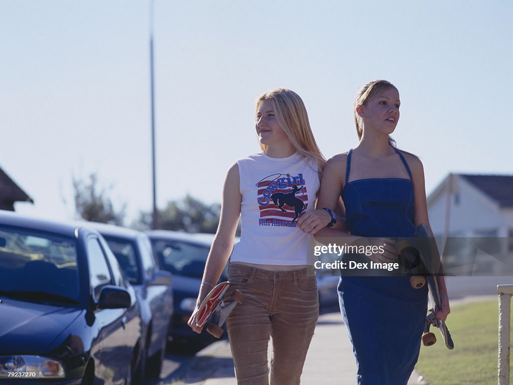 Two women walking on walkway holding skateboards