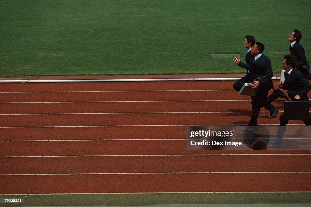 Businesspeople running on stadium track, carrying briefcases