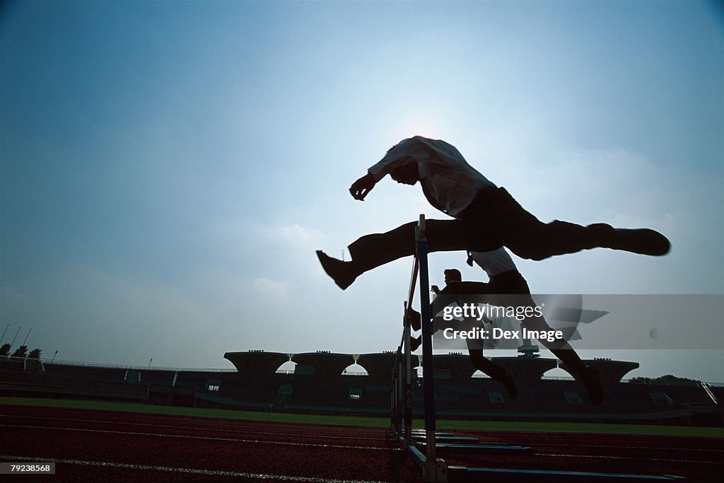 Silhouette of businessman leaping hurdle