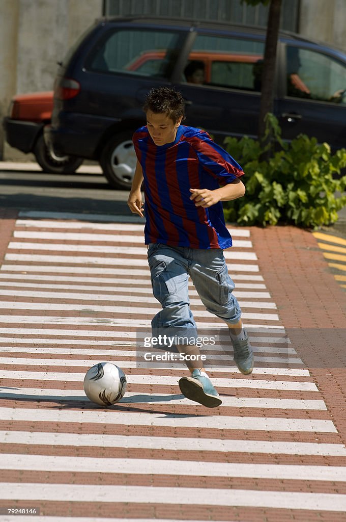 Teenage boy dribbling soccer ball in town