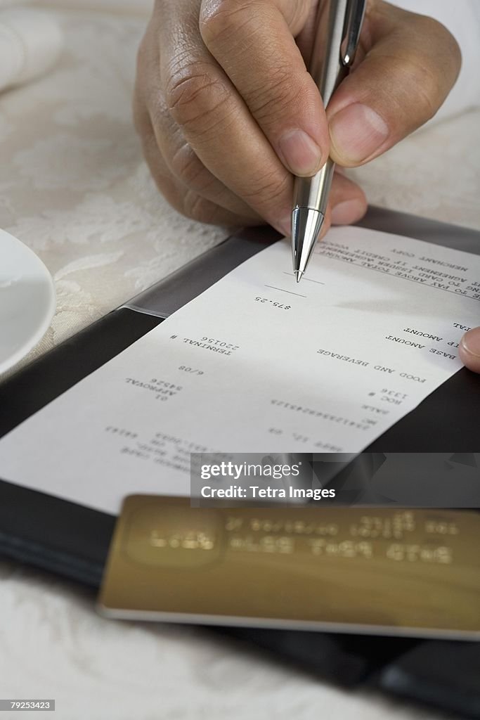 Close up of man signing credit card receipt at restaurant