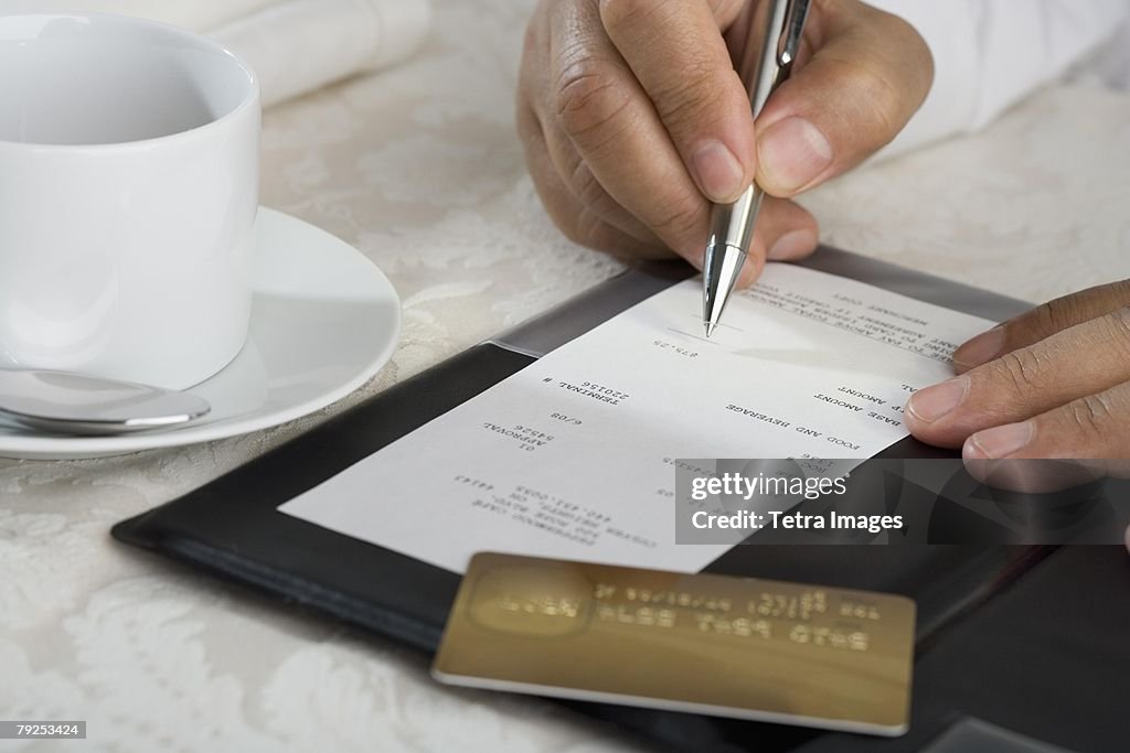 Close up of man signing credit card receipt at restaurant