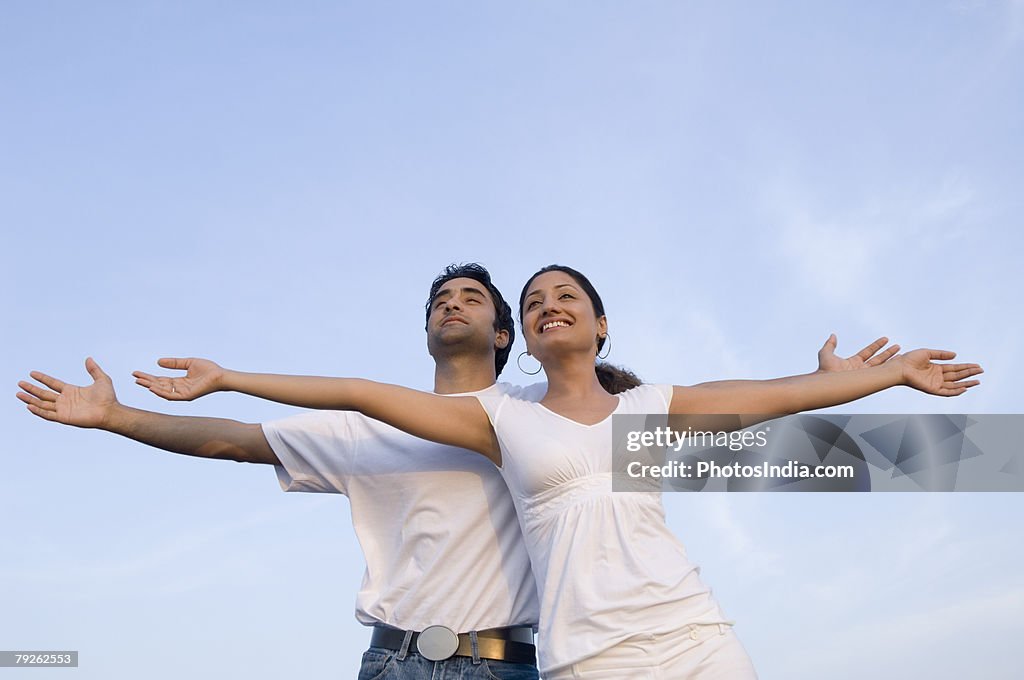 Low angle view of a young couple standing together with their arms outstretched and smiling