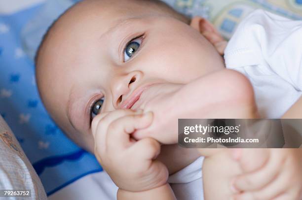 portrait of a baby lying down and sucking thumb of leg - feet sucking stock pictures, royalty-free photos & images