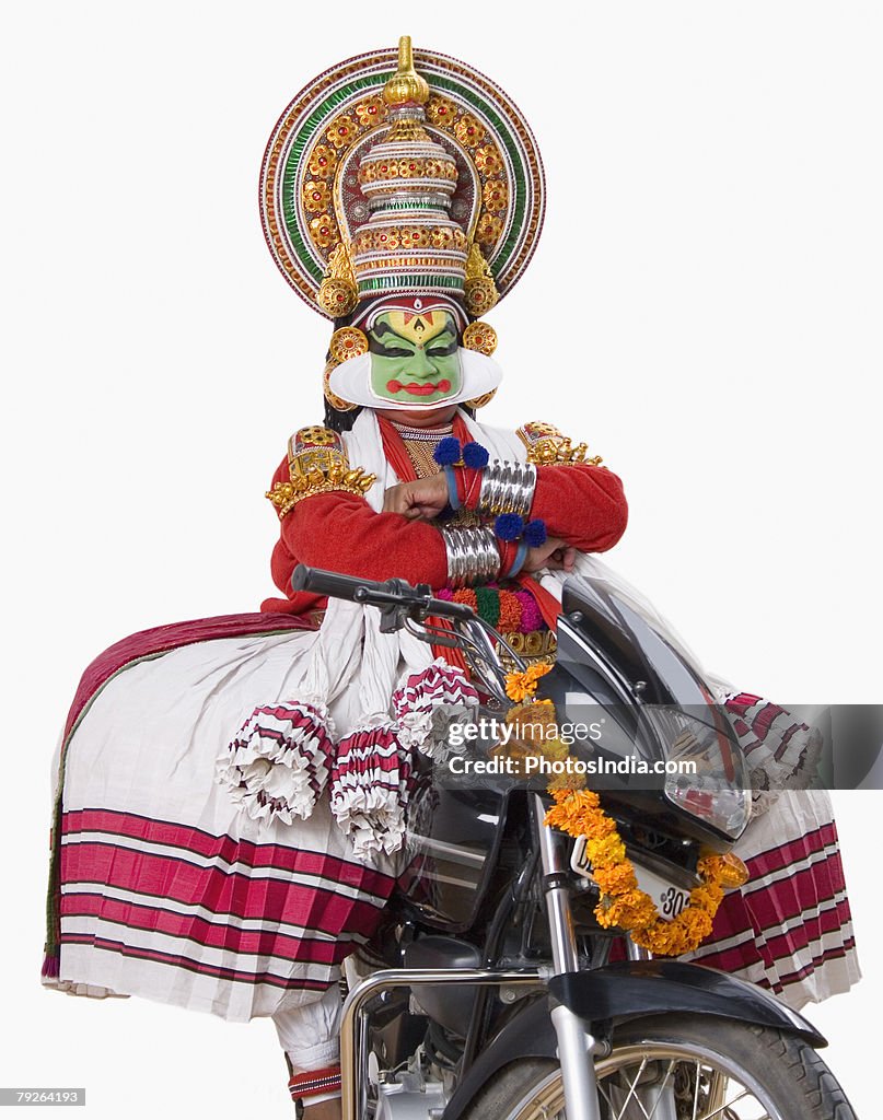 Portrait of a Kathakali dance performer sitting on a motorcycle