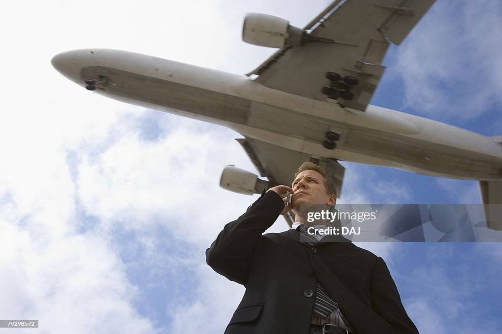A Telephone Calling Businessman with a Airplane in the Background, Low Angle View, Waist Up