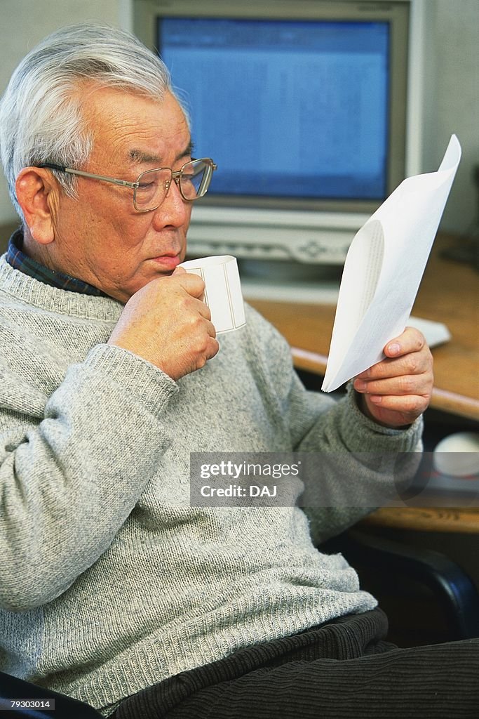 Portrait of a senior adult man reading documents with a cup in hand, Side View