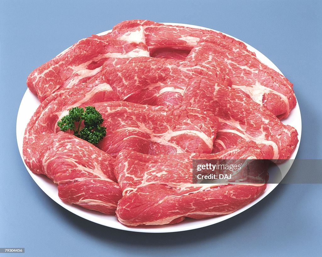 Raw beef with parsley on plate, high angle view