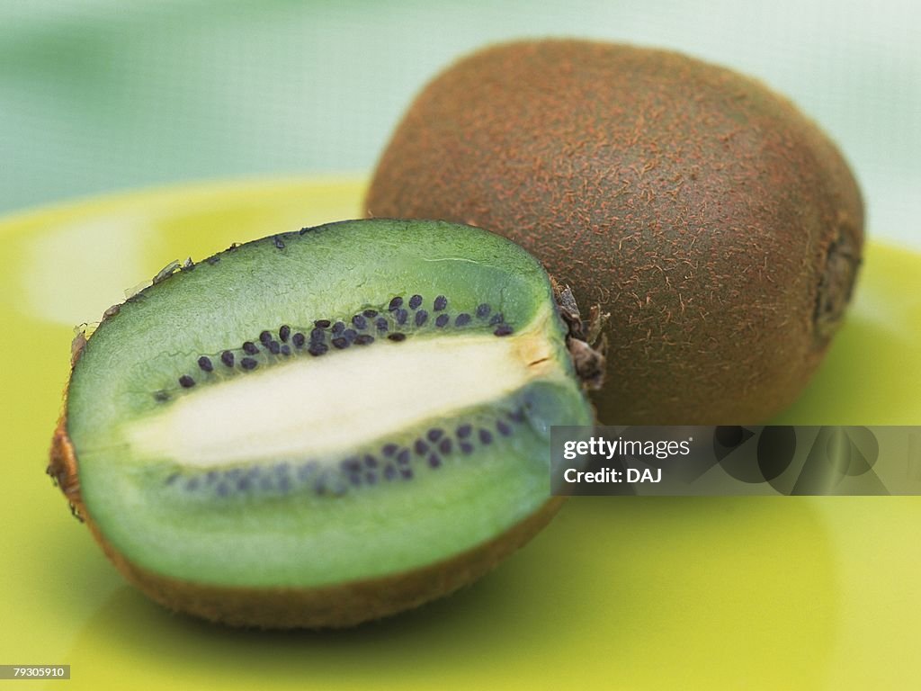 Whole and half kiwi fruits on green plate, High angle view