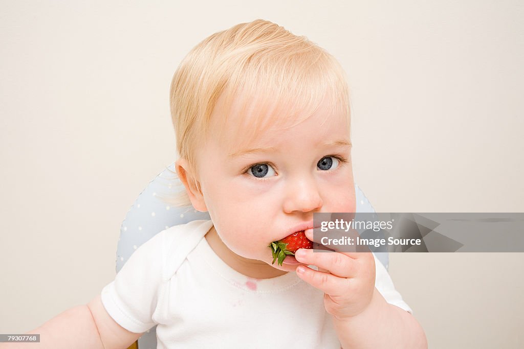 A baby boy eating a strawberry