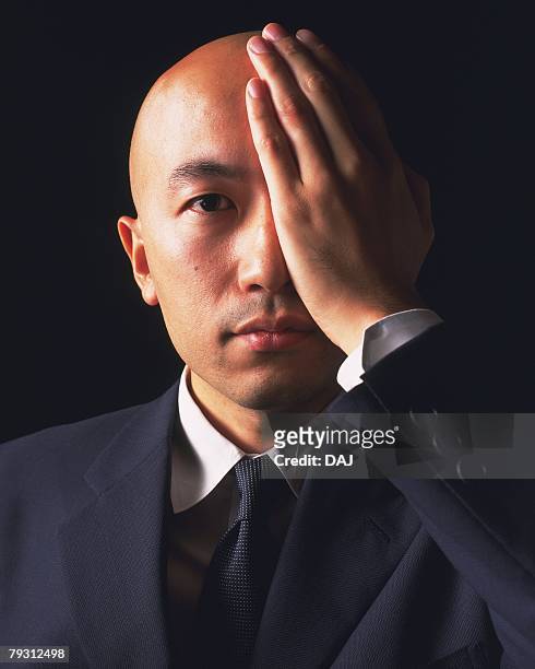 a bald headed businessman covering an eye with hand, front view - business revenge stock pictures, royalty-free photos & images