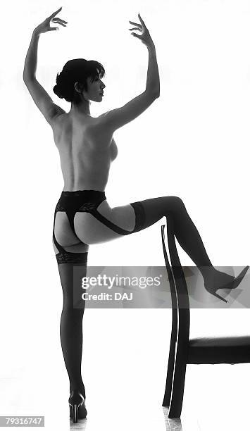 woman in garter belt and stockings, posing and putting a leg on a chair, black and white, rear view, white background - black stockings suspenders adult fotografías e imágenes de stock