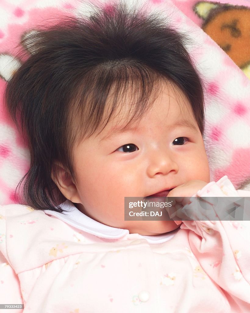 Close up of baby girl holding her finger in mouth, smiling, portrait, high angle view