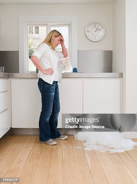 woman looking at leaking dishwasher - broken appliance stock-fotos und bilder