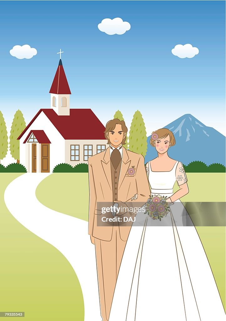 Bridal couple standing side by side in front of church, bride holding wedding bouquet, front view