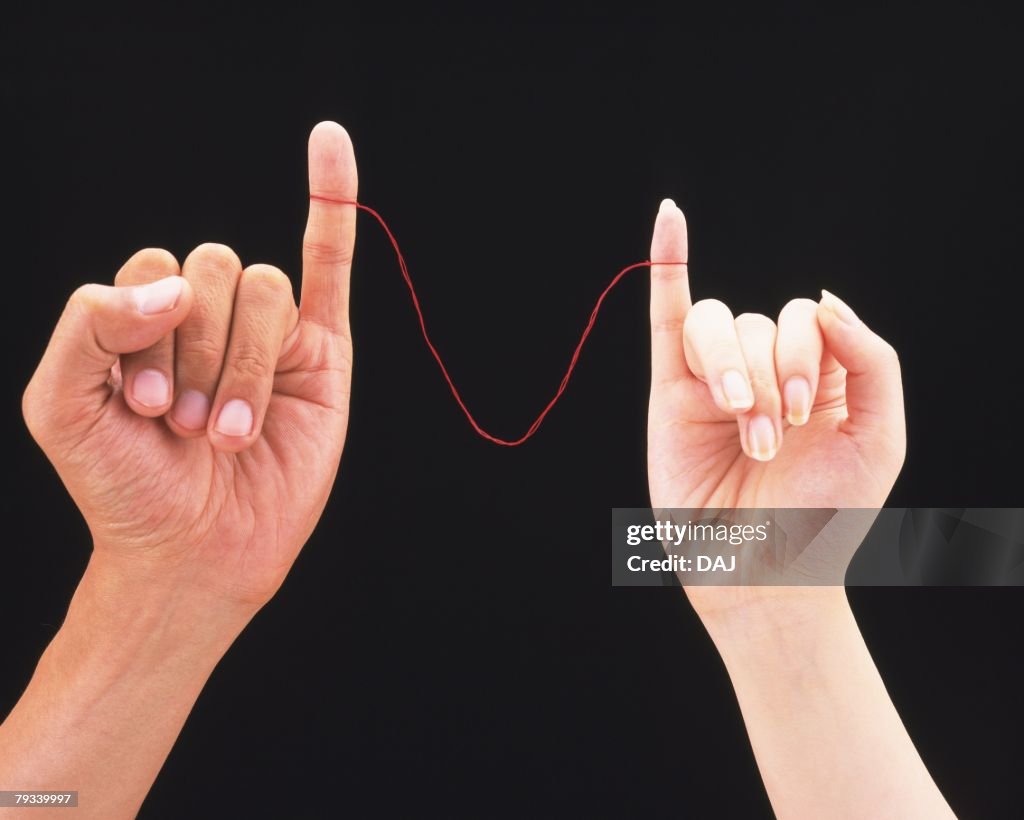 Woman and man connected by red thread tied around their pinkies