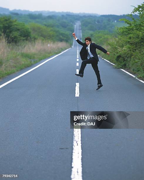 image of a businessman jumping in the air on the middle of a road, high angle view, side view - skip ストックフォトと画像