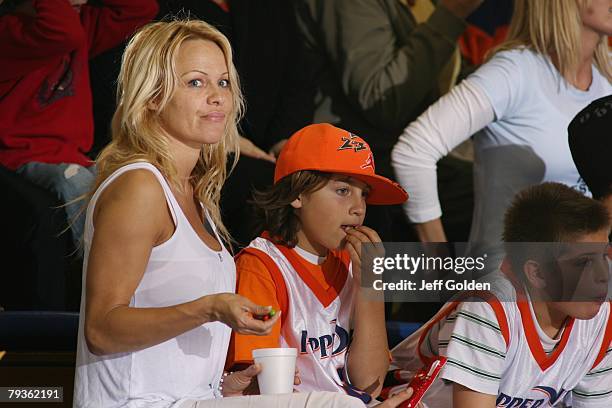 Actress Pamela Anderson eats Skittles as she sits with her son Brandon Thomas Lee before the basketball game between the Loyola Marymount Lions and...