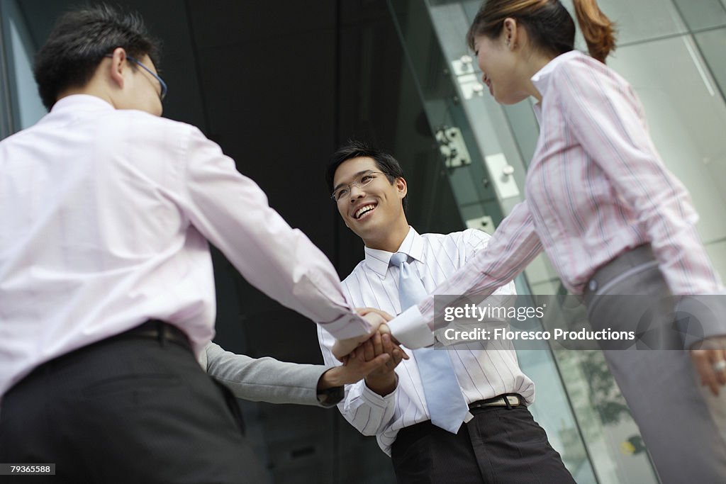 Four businesspeople outdoors with hands together in circle