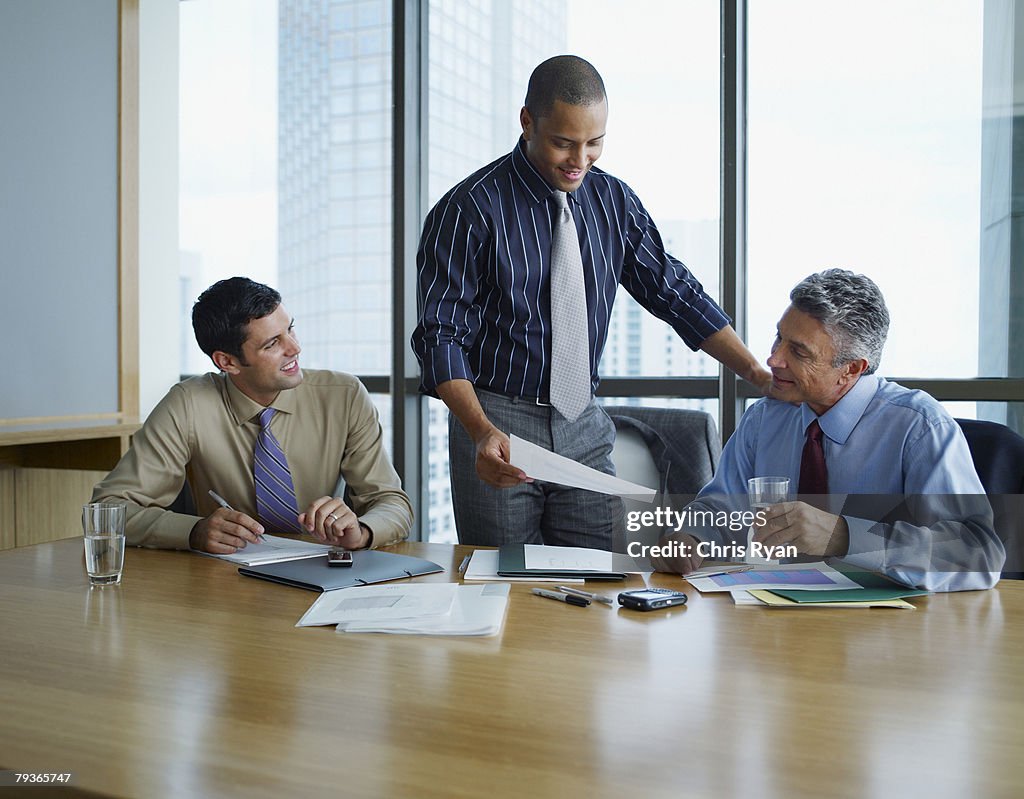 Three businessmen at a boardroom table with paperwork