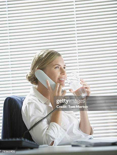 geschäftsfrau im büro am telefon mit wasser durch große fenster - wasser trinken büro stock-fotos und bilder