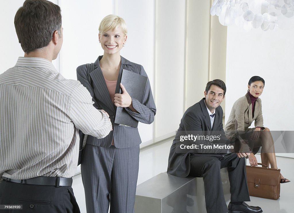 Two businesspeople shaking hands in office lobby with two businesspeople watching